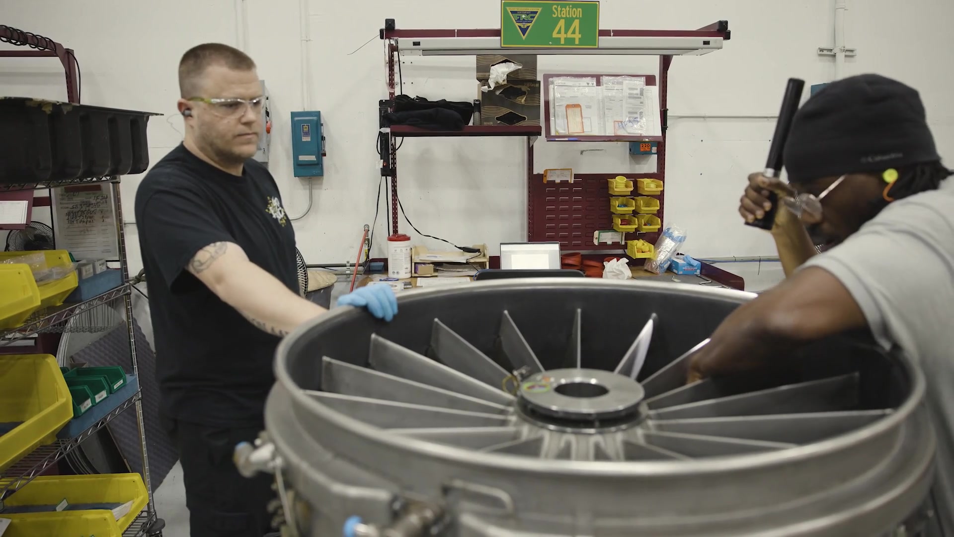 Two civilian technicians collaborate on an engine component.