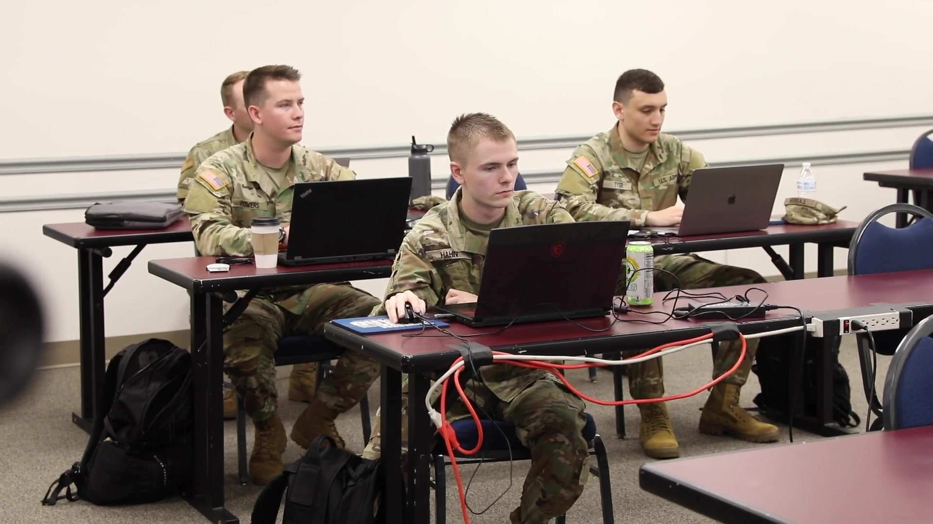 Uniformed cyber-defense participants work at laptops.