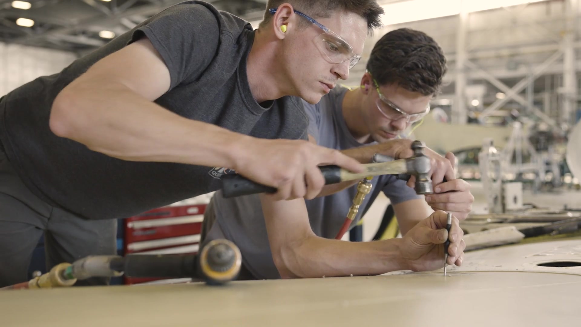 Two civilian technicians work on a sheet-metal component.
