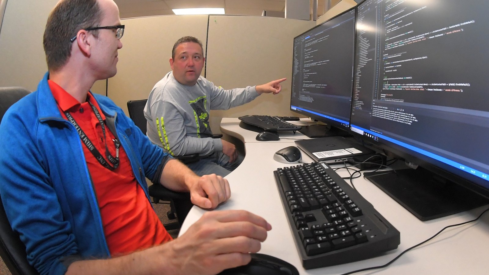 Two software teammates discuss code on large desktop monitors.