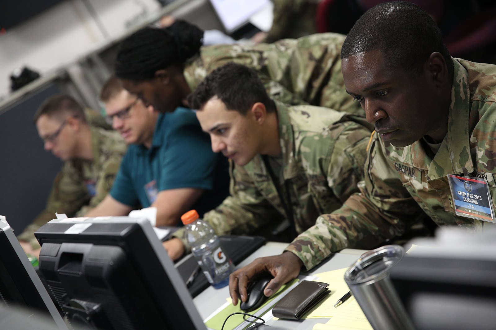 Military and civilian cyber specialists work together at desktop computers.