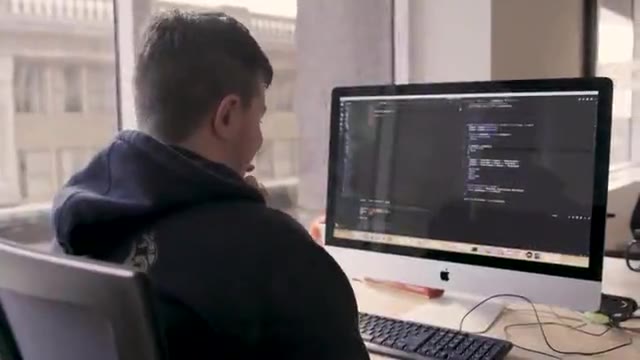 Civilian software developers collaborate at computers, review source code and discuss their work.