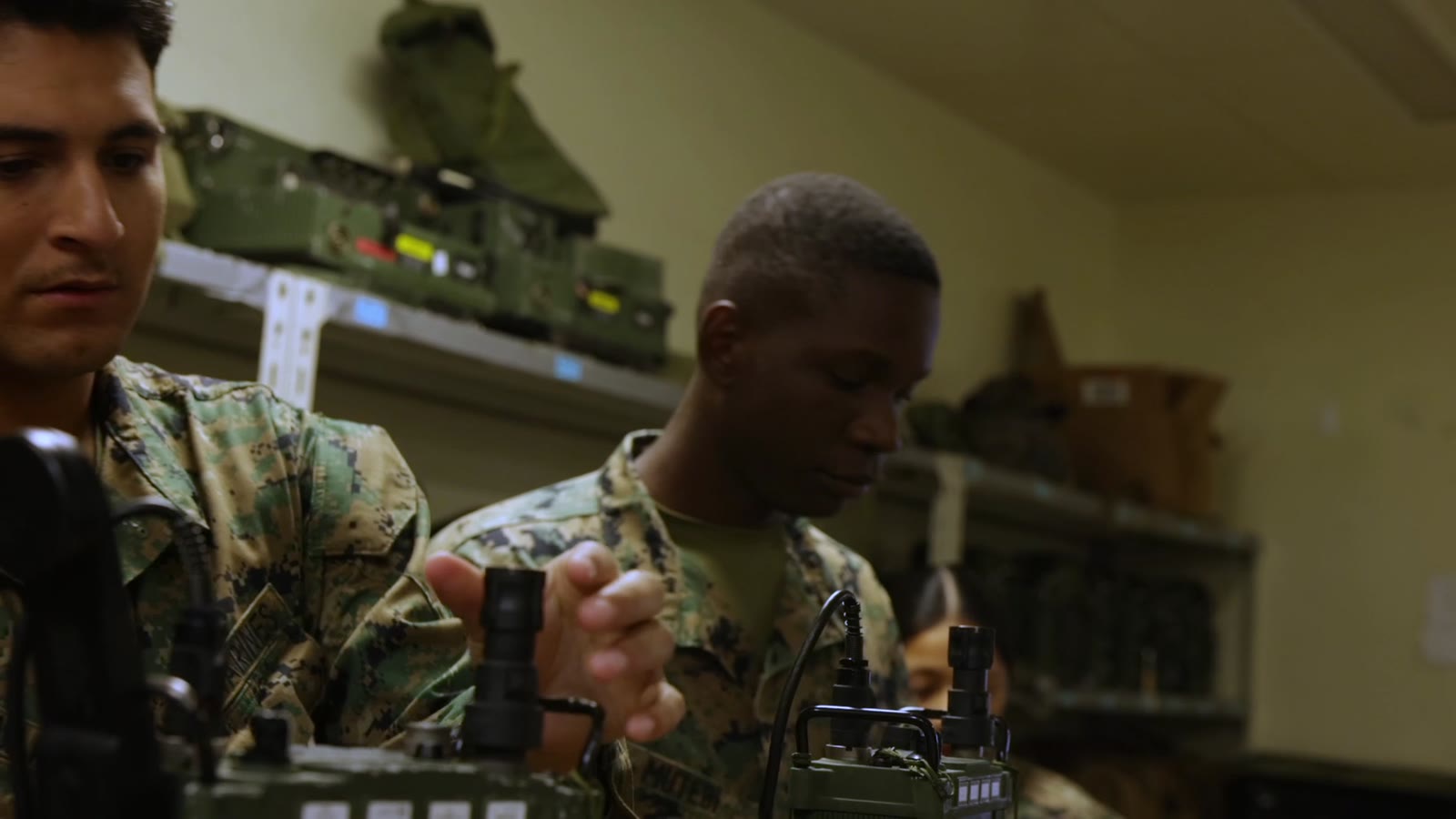 Two military communications specialists discuss a portable radio and connected test equipment.